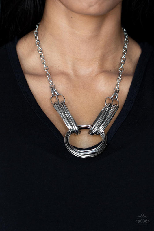 Lip Sync Links Silver Necklace - Paparazzi Accessories  Layers of oblong silver links connect to a collection of oversized textured and shiny silver rings creating a dramatic centerpiece. Attached to a silver chain, the rustic links create an unconventionally edgy statement below the collar. Features an adjustable clasp closure.  Sold as one individual necklace. Includes one pair of matching earrings.