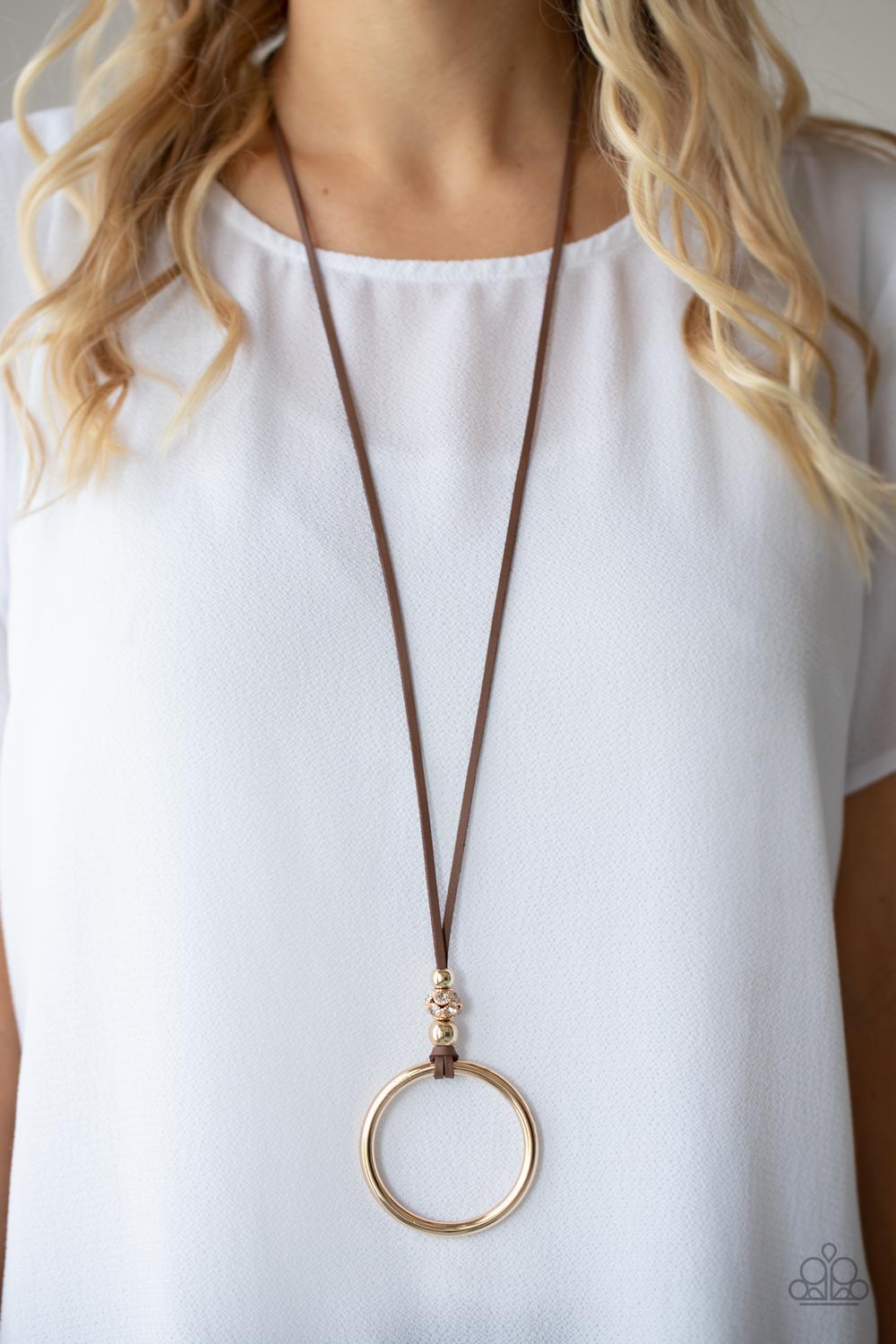 BLING Into Focus Brown Necklace - Paparazzi Accessories  Infused with pair of classic gold beads and a white rhinestone encrusted accent, lengthened brown leather cording knots around a bold gold hoop for a knockout look. Features an adjustable clasp closure.  Sold as one individual necklace. Includes one pair of matching earrings.