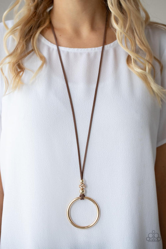 BLING Into Focus Brown Necklace - Paparazzi Accessories  Infused with pair of classic gold beads and a white rhinestone encrusted accent, lengthened brown leather cording knots around a bold gold hoop for a knockout look. Features an adjustable clasp closure.  Sold as one individual necklace. Includes one pair of matching earrings.