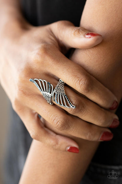 Angels Among Us Blue Ring - Paparazzi Accessories  Featuring lifelike feathery detail, two airy silver wings delicately wrap around the finger. Rows of dainty blue rhinestones adorn the winged accents, adding a celestial shimmer to the angelic centerpiece. Features a stretchy band for a flexible fit.  Sold as one individual ring.