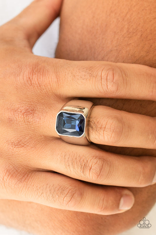 Scholar - Blue Featuring a kingly emerald style cut, an oversized blue rhinestone is pressed into the center of a glistening silver band for a statement look. Features a stretchy band for a flexible fit.  Sold as one individual ring.