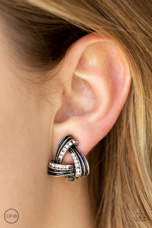Twirling Twinkle - Black Item #E313 Brushed in a shiny black finish, white rhinestone encrusted frames overlap into a bold triangular frame for a refined flair. Earring attaches to a standard clip-on earrings. All Paparazzi Accessories are lead free and nickel free!  Sold as one pair of clip-on earrings.