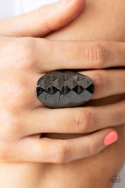Ferociously Faceted Black Ring - Paparazzi Accessories  The front of a gunmetal oval frame is faceted in a flashy geometric pattern, creating an intense industrial centerpiece around the finger. Features a stretchy band for a flexible fit.  Sold as one individual ring.