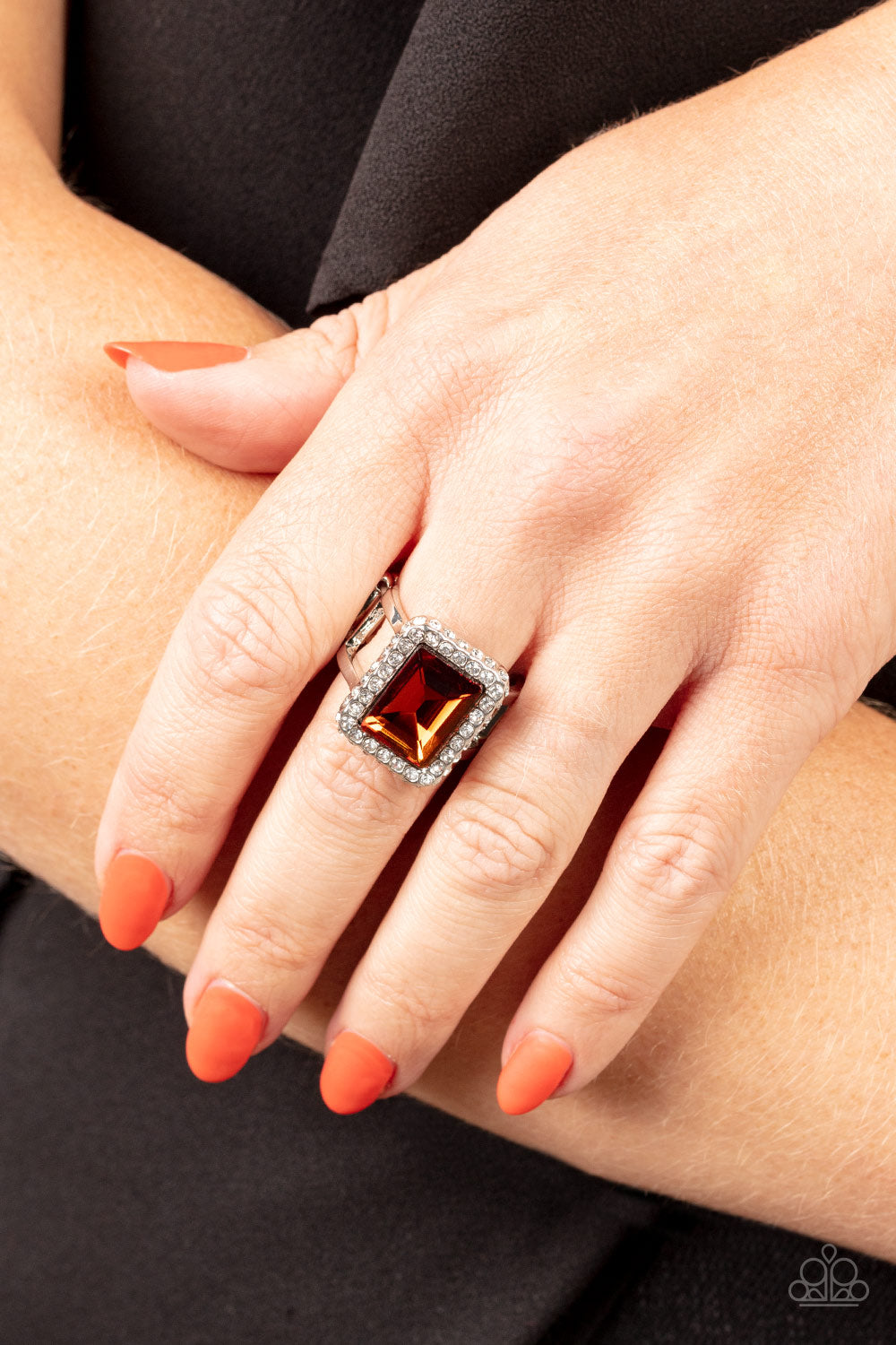 Glamorously Glitzy Brown Ring - Paparazzi Accessories  Bordered in a sparkly frame of white rhinestones, an oversized topaz emerald cut gem adorns layered silver bands atop the finger for a jaw-dropping fashion. Features a stretchy band for a flexible fit.  All Paparazzi Accessories are lead free and nickel free!  Sold as one individual ring.