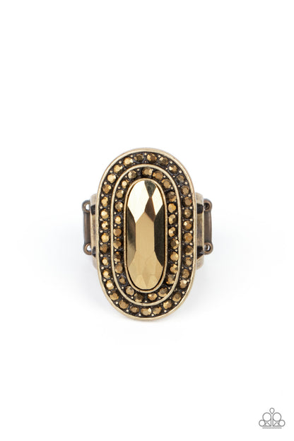 Fueled by Fashion Brass Ring - Paparazzi Accessories  An elongated sparkling aurum gem is nestled inside a linear brass frame created by double rows of dainty aurum rhinestones. The faceted gem creates a glamorously edgy effect atop the finger. Features a stretchy band for a flexible fit.  Sold as one individual ring.