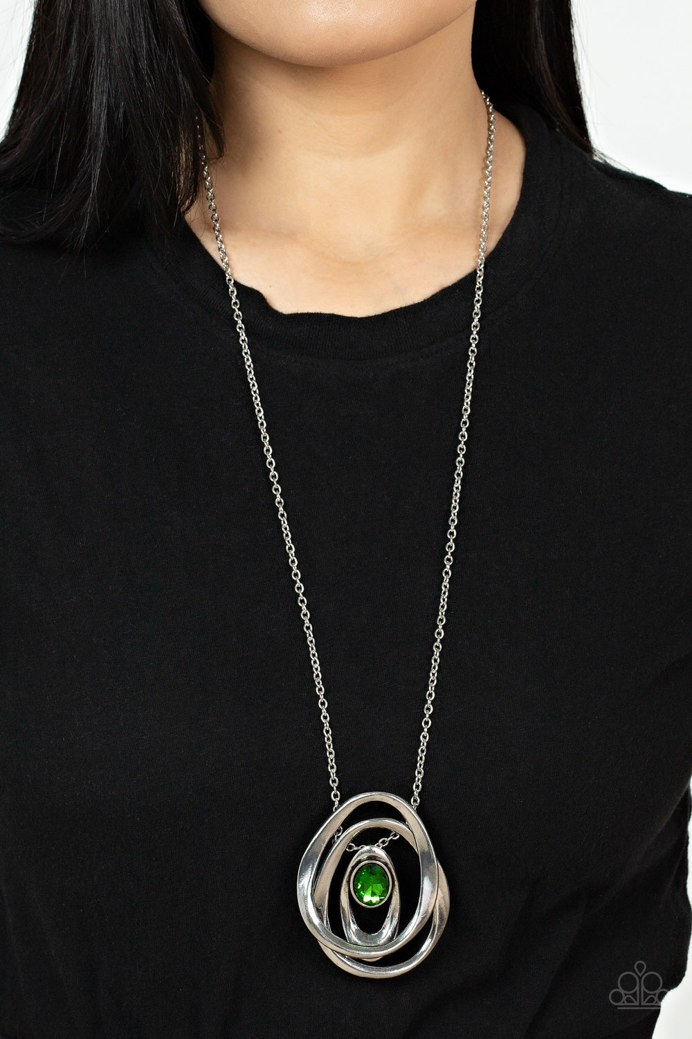 Luminous Labyrinth - Green Item #P2IN-GRXX-044XX An oversized glittery green gem seemingly floats inside an asymmetrical silver oval that glides between two oversized silver ovals at the bottom of an extended silver chain, creating an edgy pendant. Features an adjustable clasp closure.  Sold as one individual necklace. Includes one pair of matching earrings.