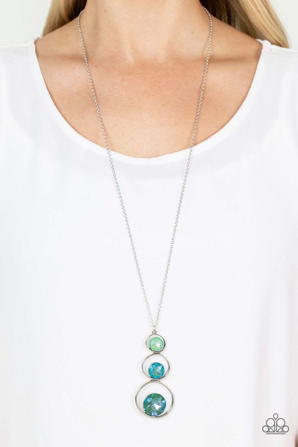 Celestial Courtier Green Necklace - Paparazzi Accessories  A sparkly ombré of opalescent green gems adorn the bottoms of three silver hoops that gradually increase in size as they stack into an asymmetrical pendant. The glowing pendant swings from the bottom of a lengthened silver chain, creating a stellar centerpiece. Features an adjustable clasp closure.  Sold as one individual necklace. Includes one pair of matching earrings.