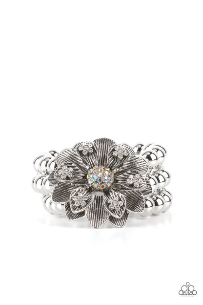 Botanical Bravado Multi Bracelet - Paparazzi Accessories  A daring oversized silver flower is composed of petals lined in antiqued silver and dotted with glistening dainty white rhinestones. A sphere of dainty iridescent rhinestones creates the center of the flower as it sits atop a trio of shiny silver beaded stretchy bands around the wrist for a dramatically whimsical look.  Sold as one individual bracelet.