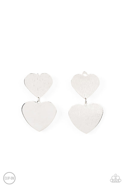 Cowgirl Crush Silver Clip-On Earring - Paparazzi Accessories  Featuring a shimmery scratched finish, an oversized silver heart charm swings from the bottom of a smaller silver heart charm, resulting in a flirtatious lure. Earring attaches to a standard clip-on fitting.  Sold as one pair of clip-on earrings.