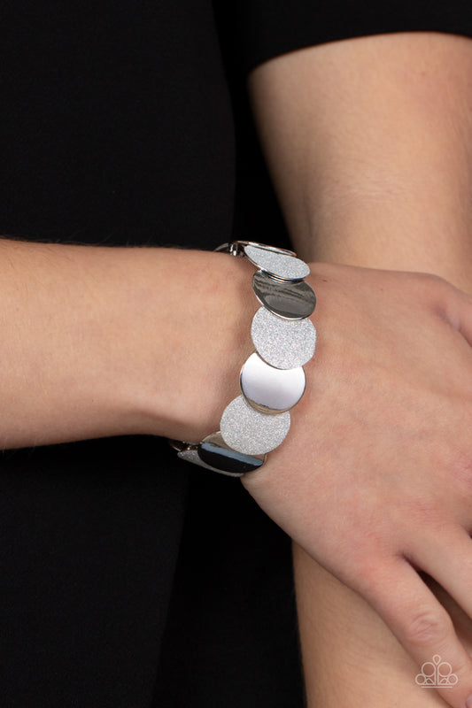 Demurely Disco Silver Bracelet - Paparazzi Accessories  A glimmering collection of shiny silver discs and glitter coated silver discs delicately overlap along stretchy bands around the wrist, creating a dazzling hint of shimmer.  Sold as one individual bracelet.