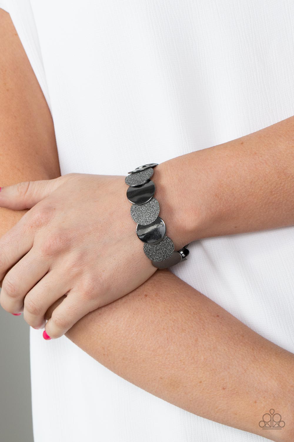 Demurely Disco - Black Item #P9BA-BKXX-089XX A glimmering collection of glistening gunmetal discs and glitter coated gunmetal discs delicately overlap along stretchy bands around the wrist, creating a dazzling hint of shimmer.  Sold as one individual bracelet.