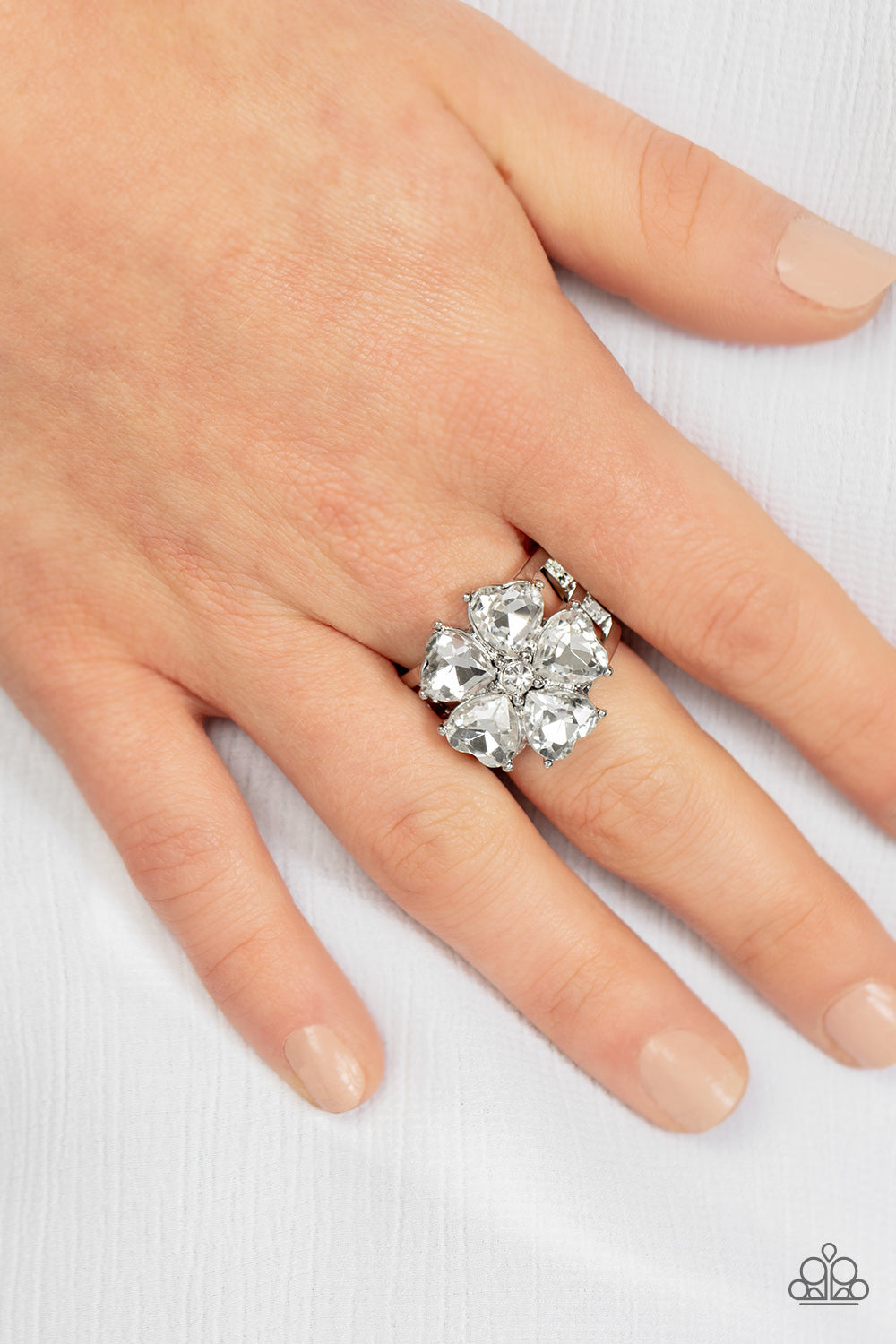 Minnesota Magic White Heart Ring - Paparazzi Accessories  Glittery white heart-shaped gems bloom from a dainty white rhinestone center, creating a sparkly floral centerpiece atop layered silver bands. Features a stretchy band for a flexible fit.  Featured inside The Preview at GLOW!  Sold as one individual ring.