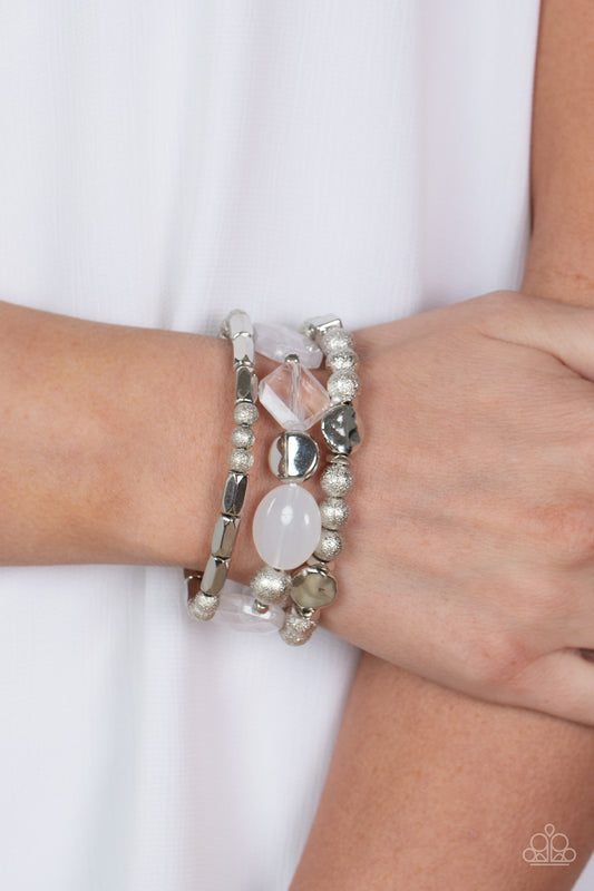 Marina Magic White Bracelet - Paparazzi Accessories  Infused with enchanting pops of white crystal-like and glassy accents, a mismatched assortment of hammered, cube, and faceted silver beads are threaded along stretchy bands around the wrist, creating shimmery layers.  Sold as one set of three bracelets.