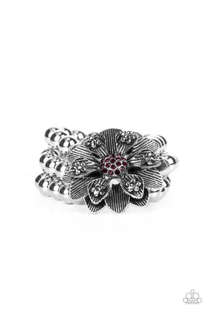 Botanical Bravado Purple Bracelet - Paparazzi Accessories  A daring oversized silver flower is composed of petals lined in antiqued silver and dotted with smoky hematite rhinestones. A sphere of dainty purple rhinestones creates the center of the flower as it sits atop a trio of shiny silver beaded stretchy bands around the wrist for a dramatically whimsical look.  Sold as one individual bracelet.