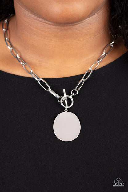 Tag Out Silver Necklace - Paparazzi Accessories  An oversized oval silver disc swings from the bottom of a substantial oval linked silver chain, resulting in a gritty industrial pendant below the collar. Features a toggle closure.  Sold as one individual necklace. Includes one pair of matching earrings.