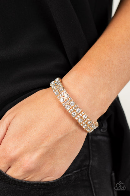 Mic Dropping Drama Gold Bracelet - Paparazzi Accessories  Pairs of glassy white rhinestones and stacked rows of glitzy white rhinestones join into studded gold frames along a stretchy band around the wrist, creating a glamorous centerpiece.  Sold as one individual bracelet.