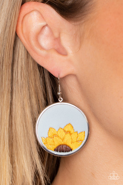 Sun-Kissed Sunflowers Blue Earring - Paparazzi Accessories  A golden yellow and brown threaded sunflower is stitched into the bottom of a blue leather frame that is encased in a sleek silver frame, resulting in a whimsical floral fashion. Earring attaches to a standard fishhook fitting.  Sold as one pair of earrings.