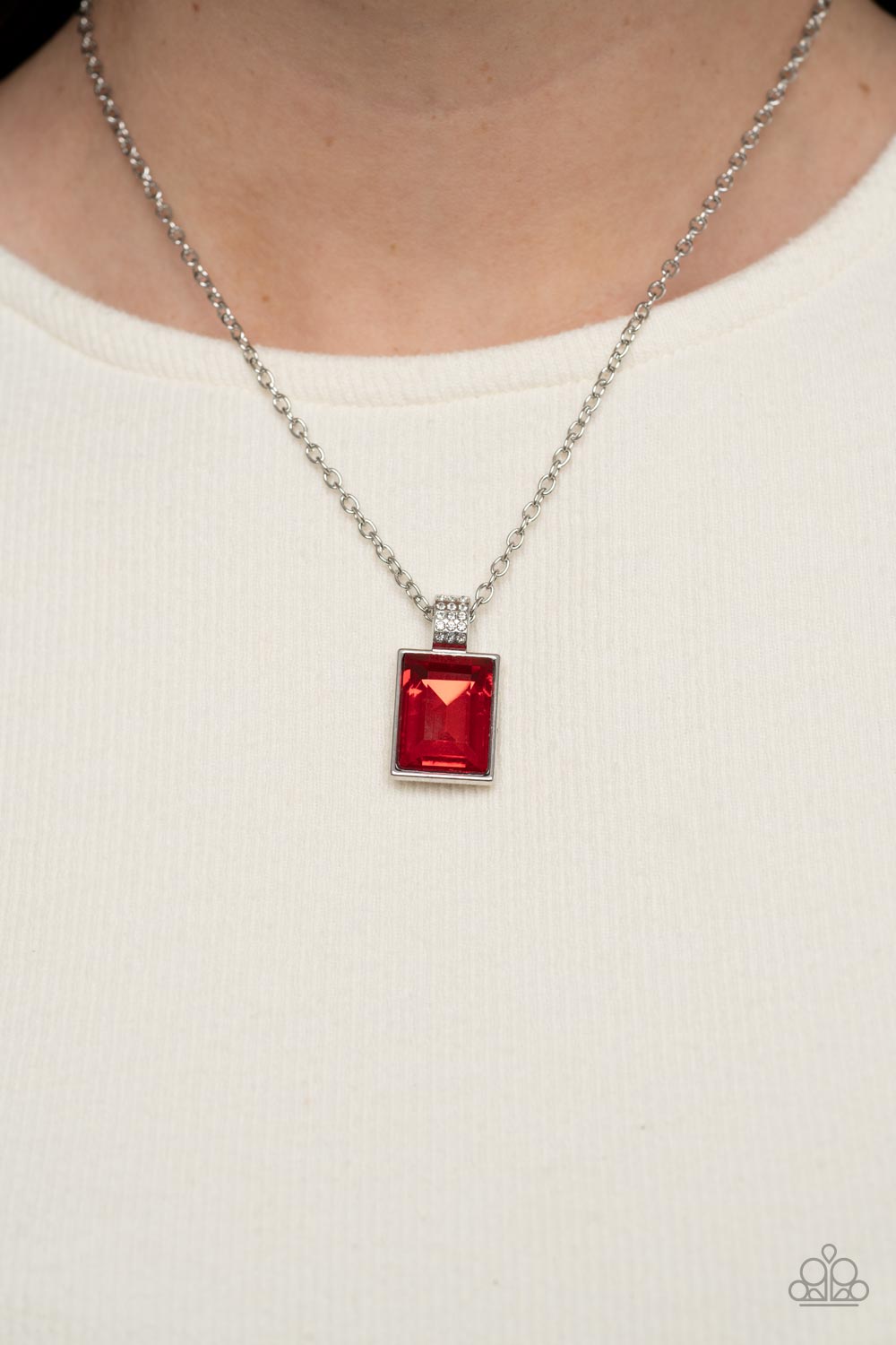 Understated Dazzle Red Necklace - Paparazzi Accessories  Featuring a white rhinestone encrusted silver fitting, an oversized emerald cut red rhinestone swings from the bottom of a dainty silver chain below the collar for a glamorous fashion. Features an adjustable clasp closure.  Sold as one individual necklace. Includes one pair of matching earrings.