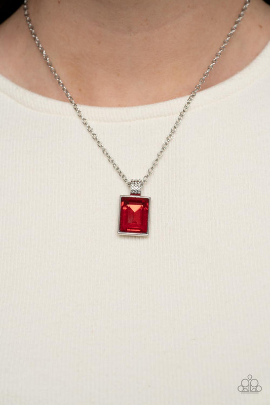 Understated Dazzle Red Necklace - Paparazzi Accessories  Featuring a white rhinestone encrusted silver fitting, an oversized emerald cut red rhinestone swings from the bottom of a dainty silver chain below the collar for a glamorous fashion. Features an adjustable clasp closure.  Sold as one individual necklace. Includes one pair of matching earrings.