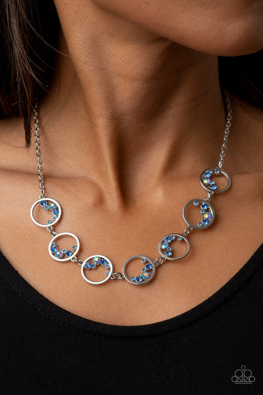 Blissfully Bubbly Blue Necklace - Paparazzi Accessories  A dainty series of shiny silver rings are sporadically dotted in bubbly rows of glassy and iridescent blue rhinestones as they delicately link below the collar, resulting in an effervescent display. Features an adjustable clasp closure.  Sold as one individual necklace. Includes one pair of matching earrings.