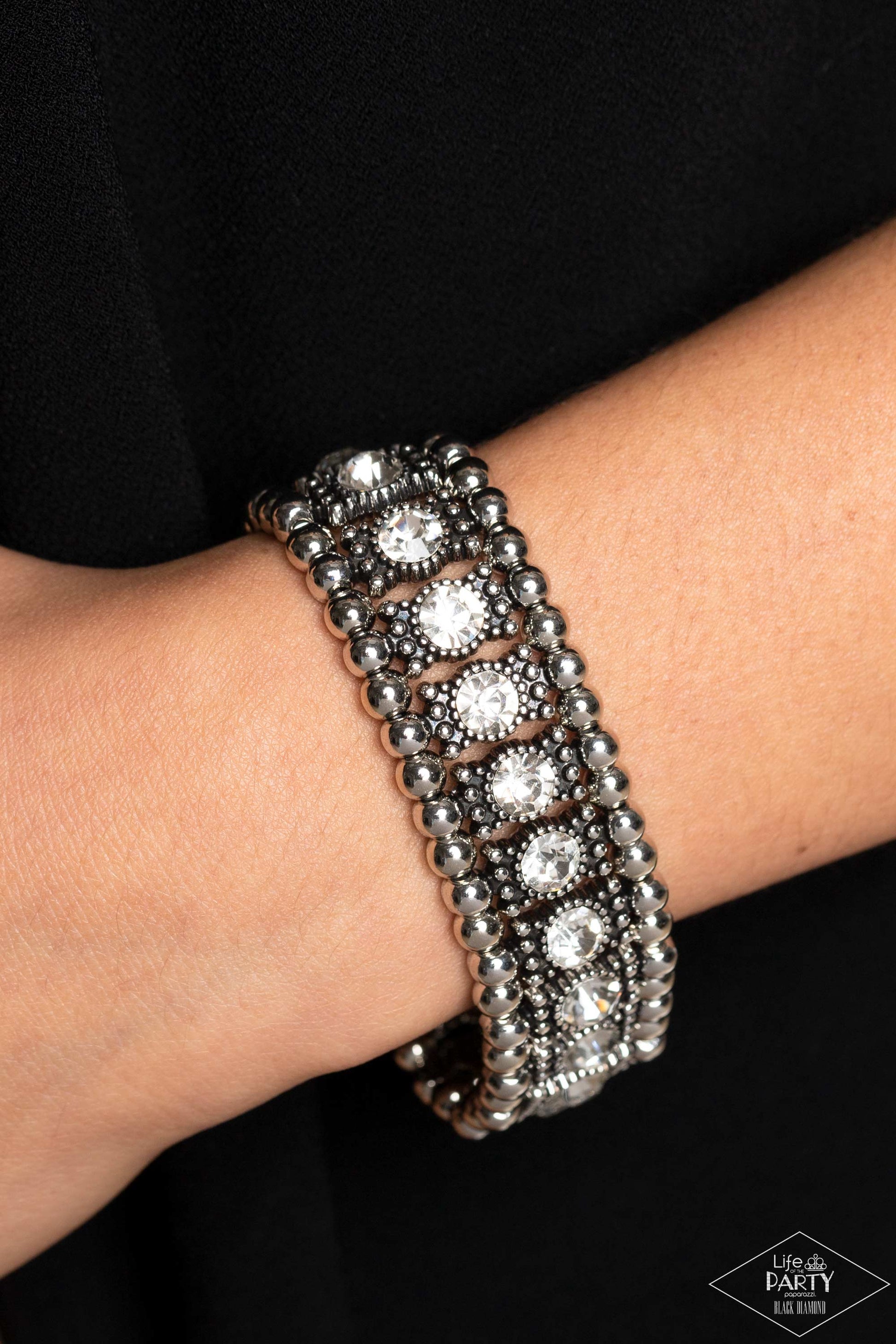 Ritzy Reboot White Bracelet - Paparazzi Accessories  A dazzling row of sparkling white rhinestones set in dotted frames is bordered by a row of dainty antiqued silver studs. Shiny round silver beads form the outermost border of this luxuriously layered design, which is threaded along stretchy bands for an upscale edgy look. P9ED-WTXX-034EE This Black Diamond Encore is back in the spotlight at the request of our 2022 Life of the Party member with Black Diamond Access, Tracey G.