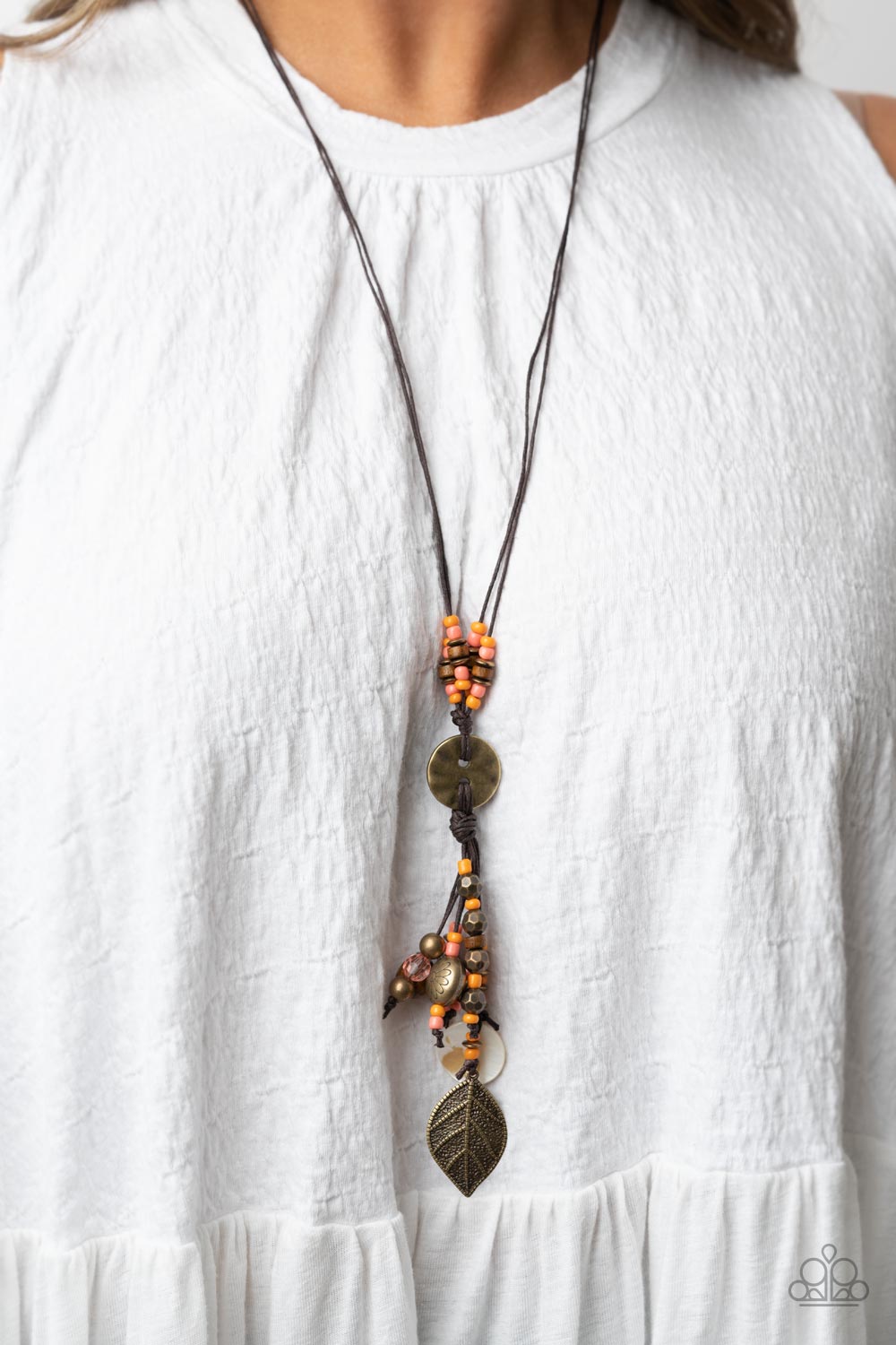 Knotted Keepsake Orange Necklace - Paparazzi Accessories  An earthy assortment of orange and coral seed beads, rustic brass discs, and wooden accents glide along lengthy strands of brown cording that knot around a hammered brass disc. Tassels of matching beads, a white shell-like accent, floral silver bead, and brass leaf charm dance from the bottom, adding playful movement to the free-spirited display. Features an adjustable clasp closure. Includes one pair of matching earrings.