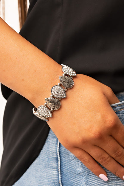 Playing Favorites White Bracelet - Paparazzi Accessories  Infused with pairs of silver beads, a decorative collection of hammered silver teardrops, and white encrusted silver teardrops alternate along stretchy bands around the wrist for an edgy flair.  Sold as one individual bracelet.