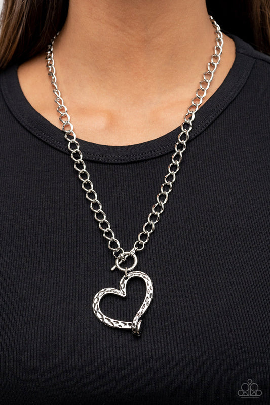 Reimagined Romance Silver Toggle Necklace - Paparazzi Accessories  A hammered silver heart frame gently twists from a toggle closure at the bottom of a chunky silver chain, resulting in a romantically rustic pendant. Features a toggle closure.  Sold as one individual necklace. Includes one pair of matching earrings.