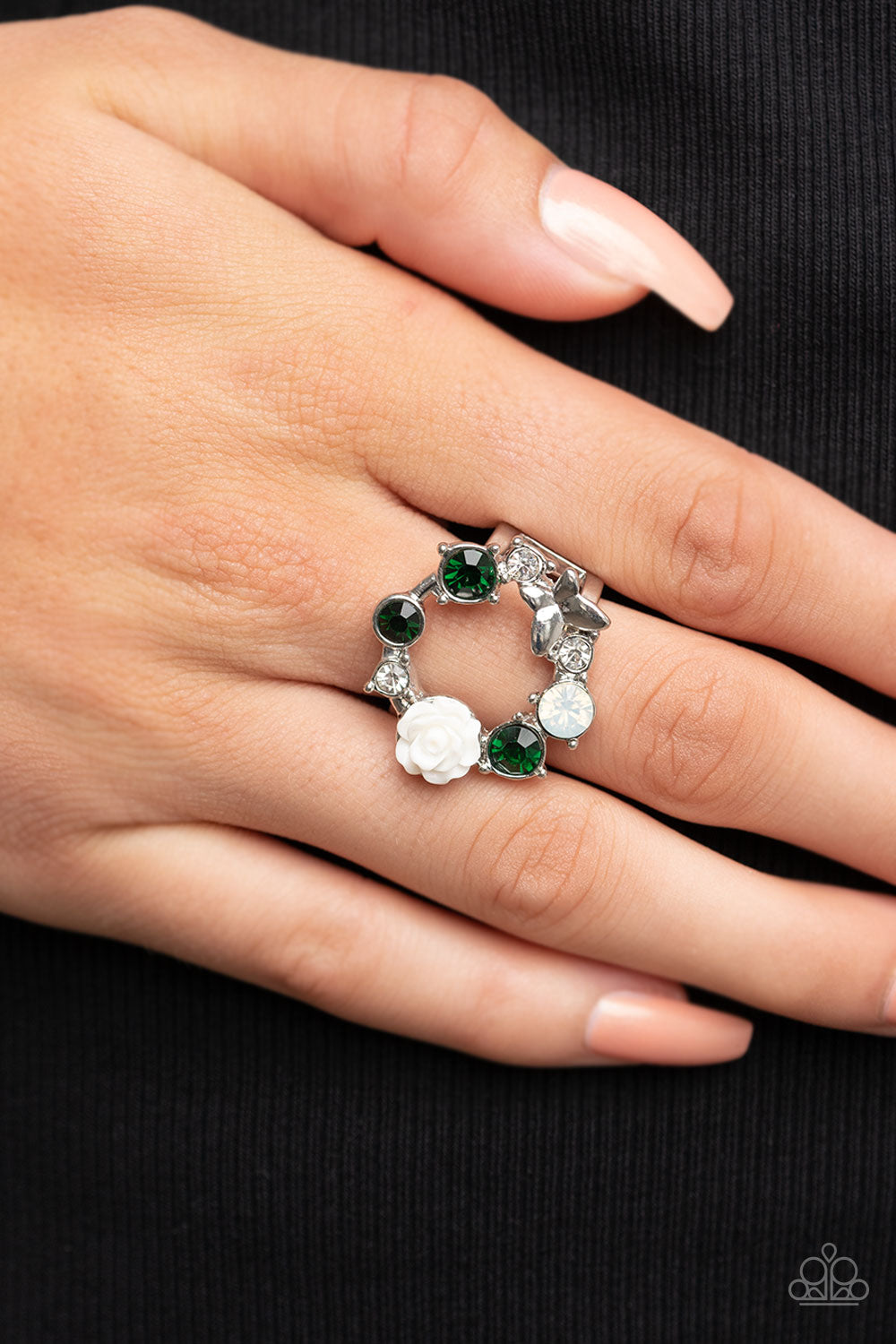 Butterfly Bustle Green Ring - Paparazzi Accessories   A glitzy collection of green, opal, and white rhinestones coalesce into a sparkly wreath atop the finger. Elegantly enhanced with a white resin rosebud, a dainty silver butterfly flutters atop the glittery centerpiece for an enchanting finish. Features a stretchy band for a flexible fit.  Sold as one individual ring.