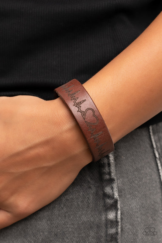 Haute Heartbeat Brown Wrap Bracelet - Paparazzi Accessories  Culminating into a heart at the center, a zigzagging pattern reminiscent of a heartbeat is etched across the front of a brown leather band around the wrist for a whimsical fashion. Features an adjustable snap closure.  Sold as one individual bracelet.