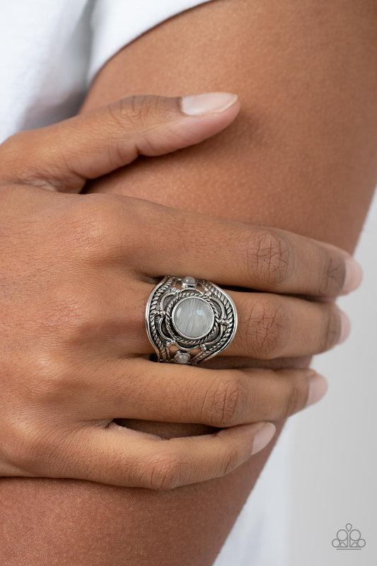 Exuberant Escapade White Ring - Paparazzi Accessories  A textured floral motif blooms around a round white cat's eye center that is flanked by two dainty white cat's eye stones, resulting in a whimsically textured centerpiece atop the finger. Features a stretchy band for a flexible fit.  Sold as one individual ring.