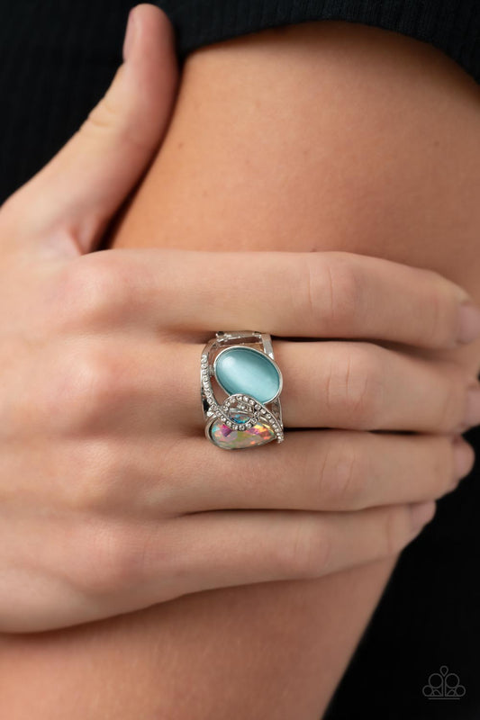 SELFIE-Indulgence Blue Ring - Paparazzi Accessories  A white rhinestone dotted silver ribbon loops and slants over a tilted blue cat's eye stone and iridescent teardrop gem, culminating into a stellar centerpiece. Features a stretchy band for a flexible fit.  Sold as one individual ring.