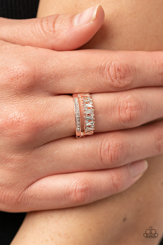 Fractal Fascination Rose Gold Ring - Paparazzi Accessories  Infused with a timeless band of white rhinestones, a dainty collection of trapezoidal cut white rhinestones staggers across the finger for a glamorously layered look. Features a dainty stretchy band for a flexible fit.  Sold as one individual ring.