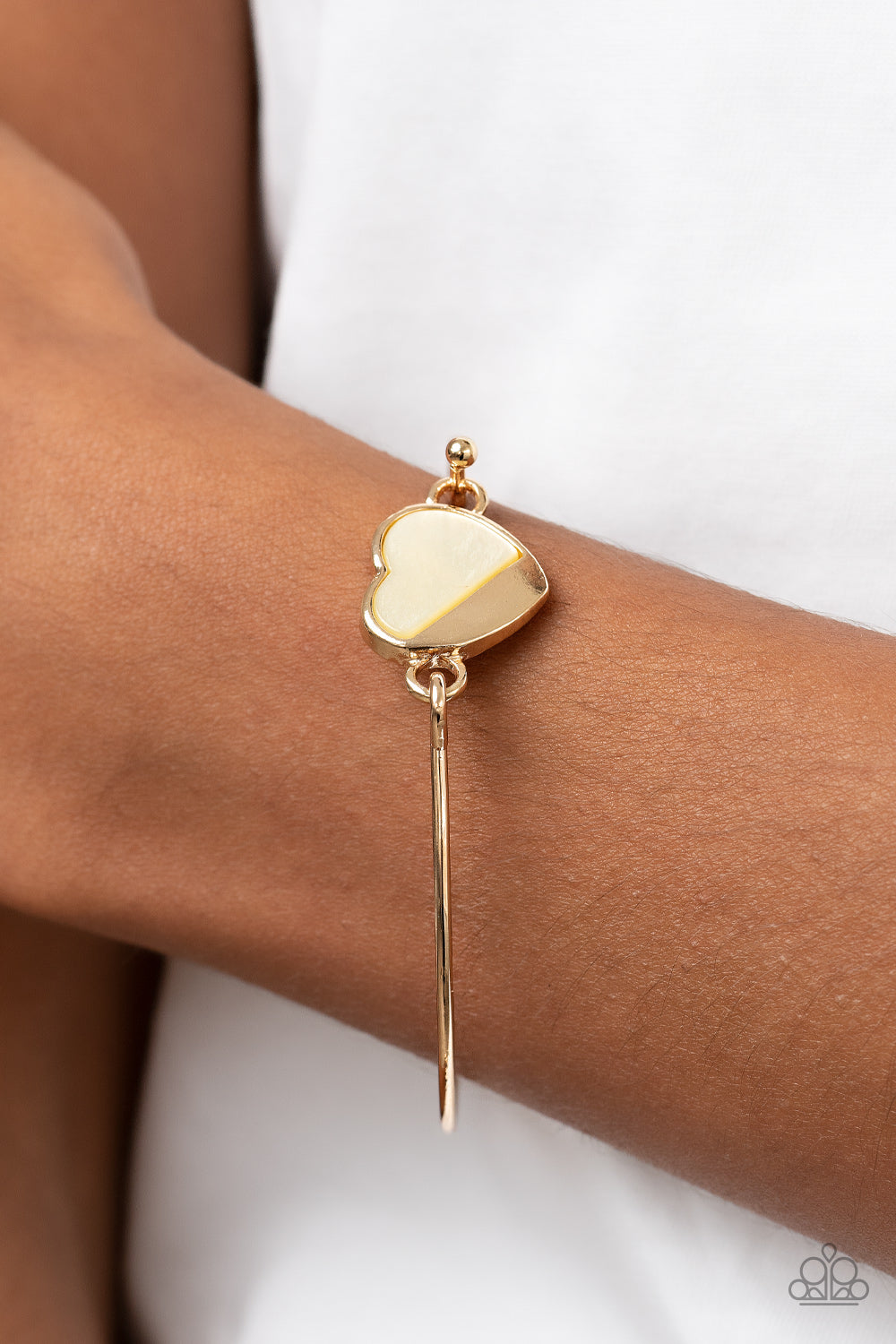 Hidden Intentions Gold Bracelet - Paparazzi Accessories  A glistening gold plate slants across a white shell-like heart charm that delicately hinges to a dainty gold bangle-like bracelet, creating a charming centerpiece around the wrist. Features a barbell closure.  Sold as one individual bracelet.
