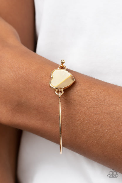 Hidden Intentions Gold Bracelet - Paparazzi Accessories  A glistening gold plate slants across a white shell-like heart charm that delicately hinges to a dainty gold bangle-like bracelet, creating a charming centerpiece around the wrist. Features a barbell closure.  Sold as one individual bracelet.