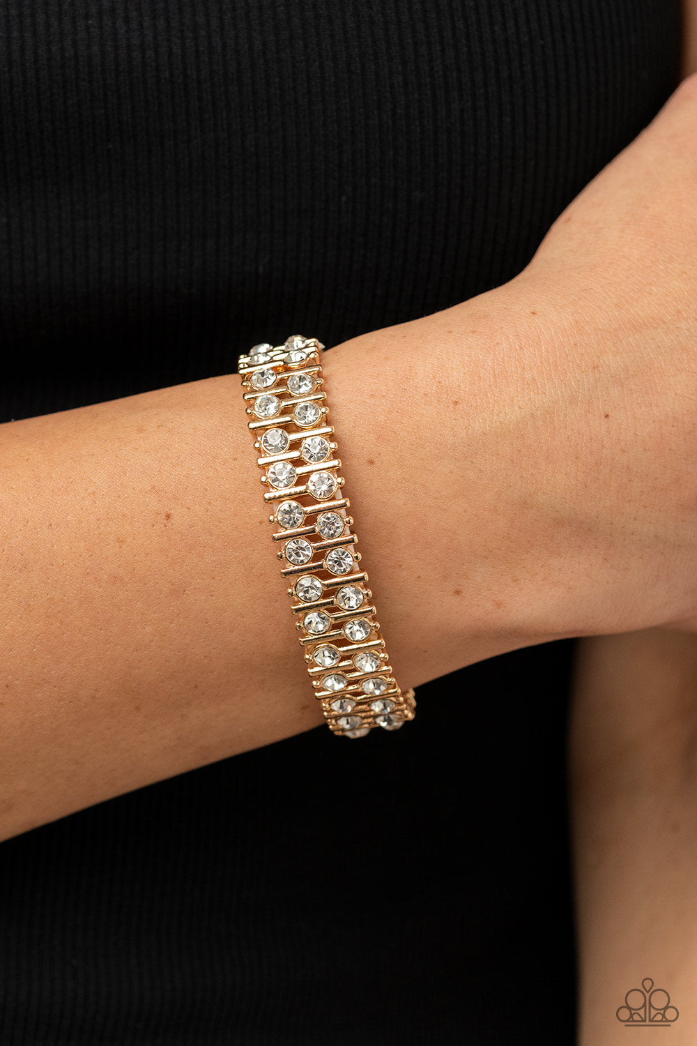 Generational Glimmer Gold Bracelet - Paparazzi Accessories  Attached to gold bars, a staggered display of solitaire white rhinestones alternates along a stretchy band around the wrist for an unexpected pop of shimmer around the wrist.  Sold as one individual bracelet.