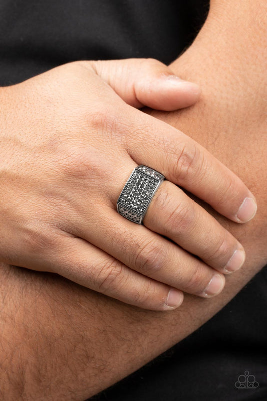The front of a rectangular silver frame is encrusted in sections of hematite rhinestones, resulting in a smoldering centerpiece atop the finger. Features a stretchy band for a flexible fit.  Sold as one individual ring.