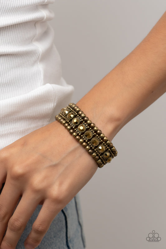 Ritzy Reboot Brass Bracelet - Paparazzi Accessories  A dazzling row of gritty aurum rhinestones set in dotted frames is bordered by a row of dainty antiqued brass studs. Rustic brass beads form the outermost border of this luxuriously layered design, which is threaded along stretchy bands for an upscale edgy look.  Sold as one individual bracelet.
