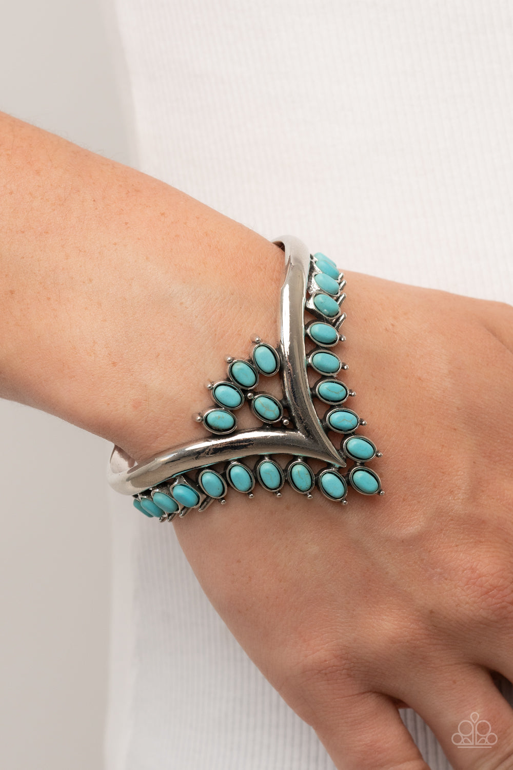 Teton Tiara Blue Cuff Bracelet - Paparazzi Accessories  Turquoise oval stones, encased in studded silver frames, line the edge of a daring V-shaped silver cuff. A gathering of turquoise stones adorns the center of the bracelet, adding a finishing touch to the rustically regal cuff.  Sold as one individual bracelet.