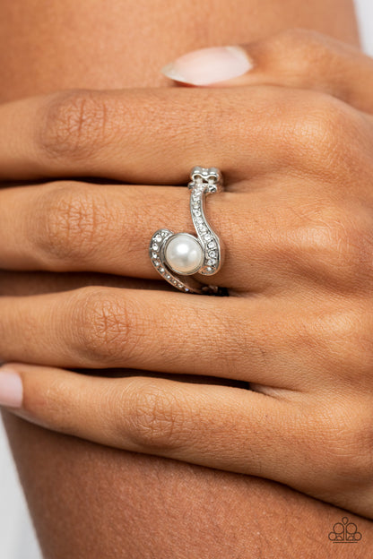 Envious Enrapture White Ring - Paparazzi Accessories   A bubbly white pearl seemingly balances between two swooping silver ribbons dotted in dainty white rhinestones, resulting in a timeless centerpiece atop the finger. Features a dainty stretchy band for a flexible fit.  Sold as one individual ring.