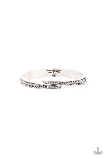 Deco Drama Silver Hinge Bracelet - Paparazzi Accessories  Encrusted in stacked sections of antiqued silver studs and smoky hematite rhinestones, two silver bars delicately overlap at the center of the wrist, resulting in an edgy cuff-like bangle. Features a hinged closure.  Sold as one individual bracelet.