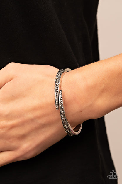 Deco Drama Silver Hinge Bracelet - Paparazzi Accessories  Encrusted in stacked sections of antiqued silver studs and smoky hematite rhinestones, two silver bars delicately overlap at the center of the wrist, resulting in an edgy cuff-like bangle. Features a hinged closure.  Sold as one individual bracelet.