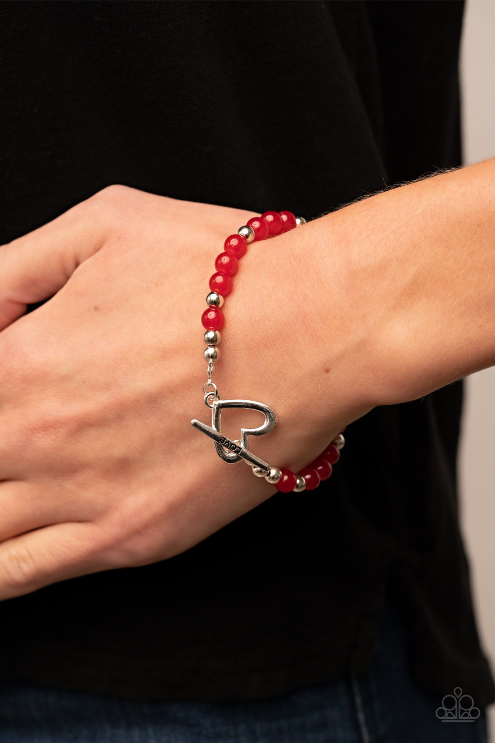 Following My Heart Red Bracelet - Paparazzi Accessories  A shiny silver heart frame interlocks with a toggle closure at the center of a shiny silver and glassy red beaded bracelet. The silver toggle is stamped in the word, "love," for a romantic finish. Features a toggle closure.  Sold as one individual bracelet.