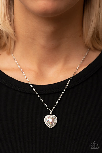 Taken with Twinkle Multi Necklace - Paparazzi Accessories  Bordered in stacked rows of glassy white rhinestones, a twinkly iridescent heart shaped gem sparkles at the center of a dainty silver chain for a flirtatious fashion. Features an adjustable clasp closure.  Sold as one individual necklace. Includes one pair of matching earrings.