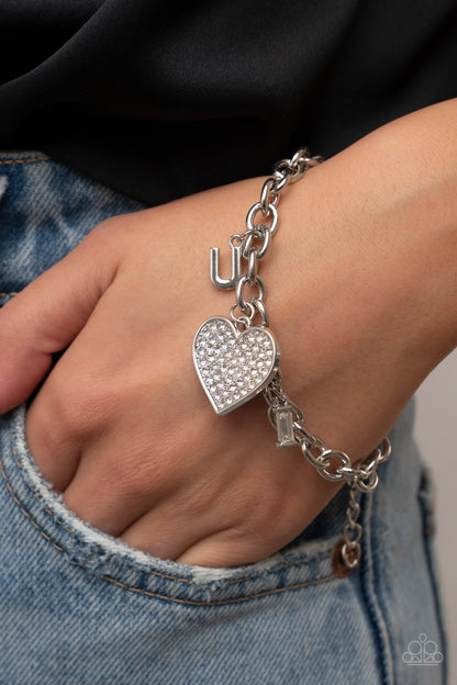 Letters of Love White Necklace & Bracelet Set - Paparazzi Accessories Encrusted with sparkly white rhinestones, an oversized silver heart charm dances between a pair of "I" and "U" charms, resulting in a heartwarming message along a dainty silver chain across the chest and around the wrist. Sold as one individual necklace. Includes one matching bracelet. Get The Complete Look! Bracelet: "Declaration of Love - White"