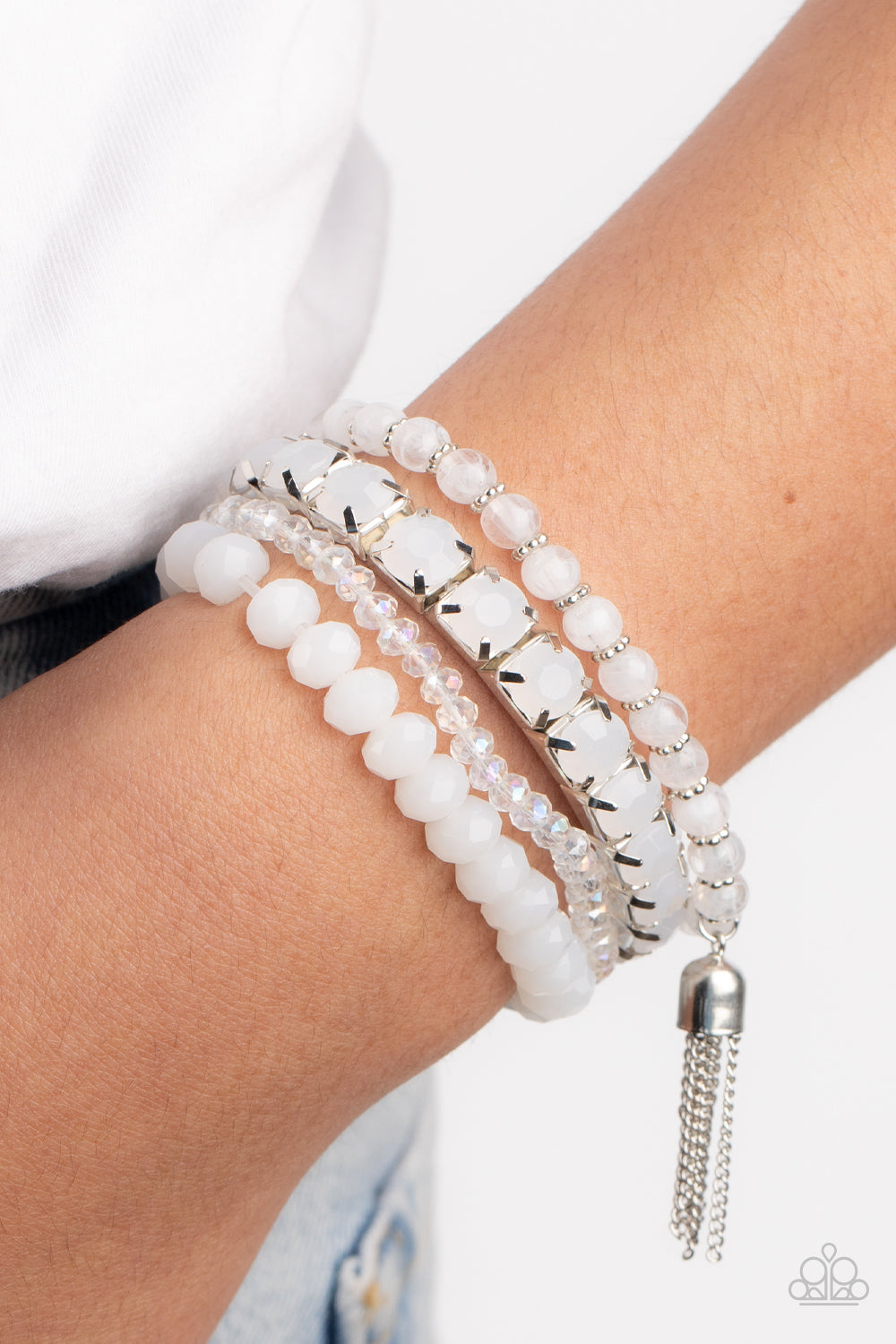Day Trip Trinket White Bracelet - Paparazzi Accessories  Pinched in silver fittings, a stretchy band of dewy white beads joins mismatched strands of cloudy and glassy white crystal-like and stretchy bracelets around the wrist. A single silver chain tassel dances from the crystalline compilation for a final flirty finesse.  Sold as one set of four bracelets.