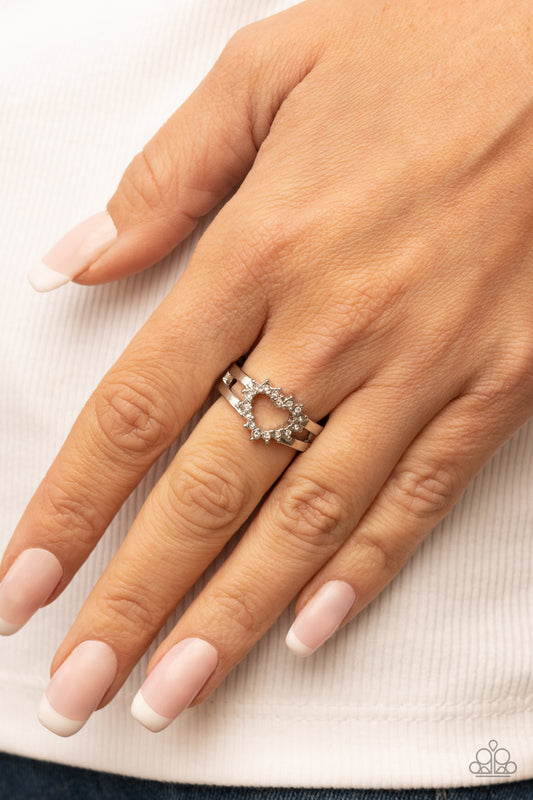 First Kisses White Ring - Paparazzi Accessories  White rhinestone pronged silver fittings coalesce into an airy heart frame atop the center of layered silver frames, resulting in a romantic centerpiece atop the finger. Features a dainty stretchy band for a flexible fit.  Sold as one individual ring.