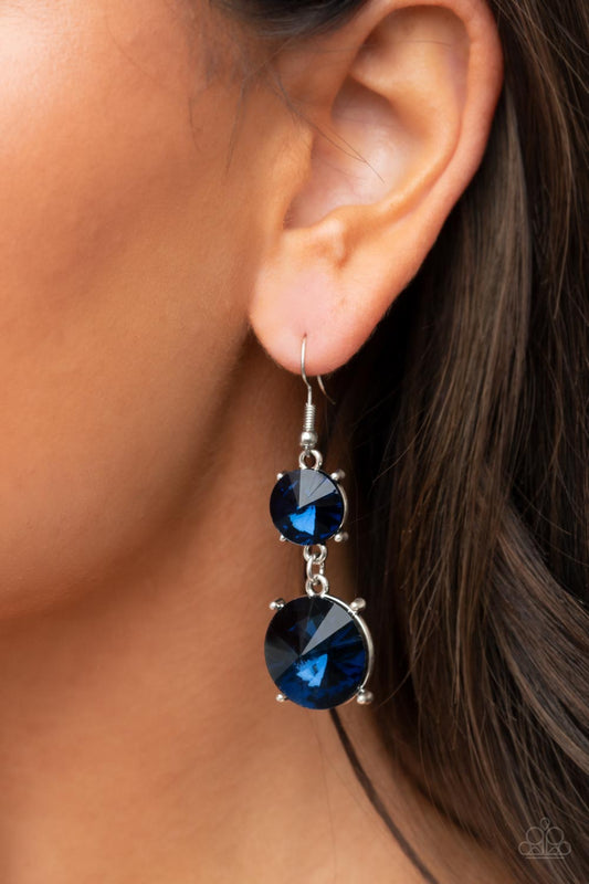 Sizzling Showcase Blue Earring - Paparazzi Accessories  Featuring pronged silver fittings, two oversized blue rhinestones dramatically link into a bold smoldering lure as they drip dazzlingly from the ear. Earring attaches to a standard fishhook fitting.  Sold as one pair of earrings.