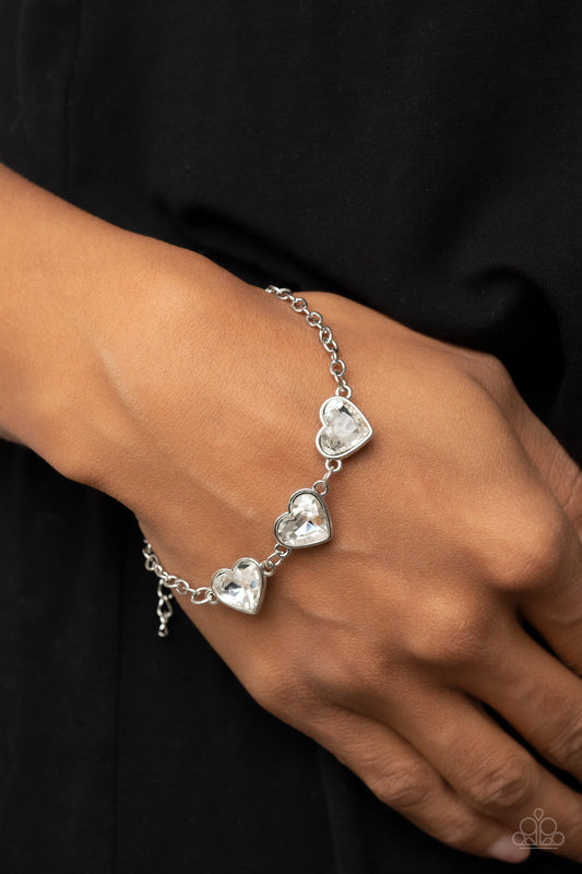 Little Heartbreaker White Bracelet - Paparazzi Accessories  Nestled in silver frames, a trio of glittery white heart-shaped gems delicately links across the wrist for a dash of swoon-worthy shimmer. Features an adjustable clasp closure.  Sold as one individual bracelet.
