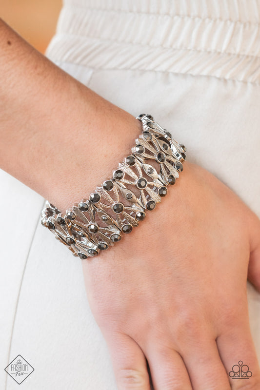 Thematic Twinkle Silver Bracelet - Paparazzi Accessories  Dotted with layers of smoky hematite rhinestones, flared and textured silver bars crisscross and merge into shiny silver frames. Threaded along stretchy bands, the smoldering frames create an intensely swanky fashion around the wrist.  Sold as one individual bracelet.